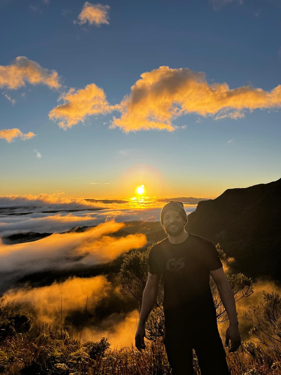 Geo sorrindo no alto da serra, acima das nuvens, ao pôr do sol